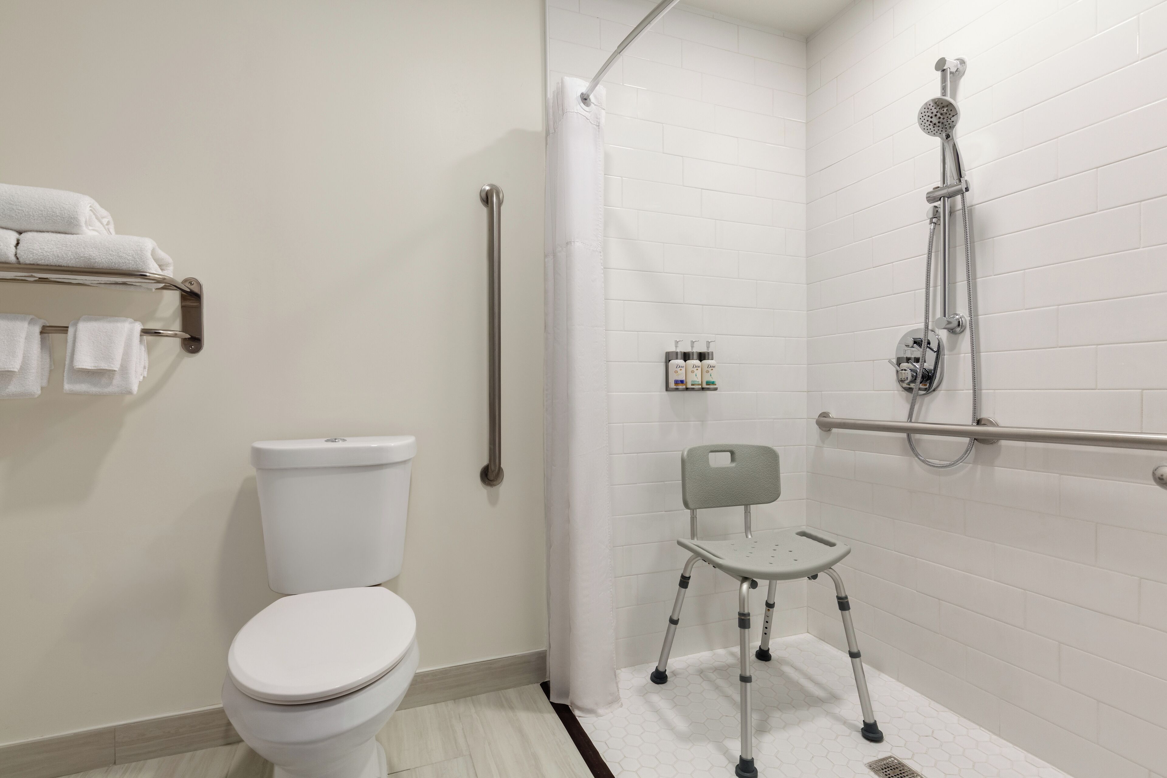 A modern bathroom with a white toilet, a shower with a handheld showerhead, a grab bar, and a wheelchair-accessible chair.