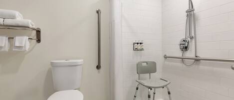 A modern bathroom with a white toilet, a shower with a handheld showerhead, a grab bar, and a wheelchair-accessible chair.