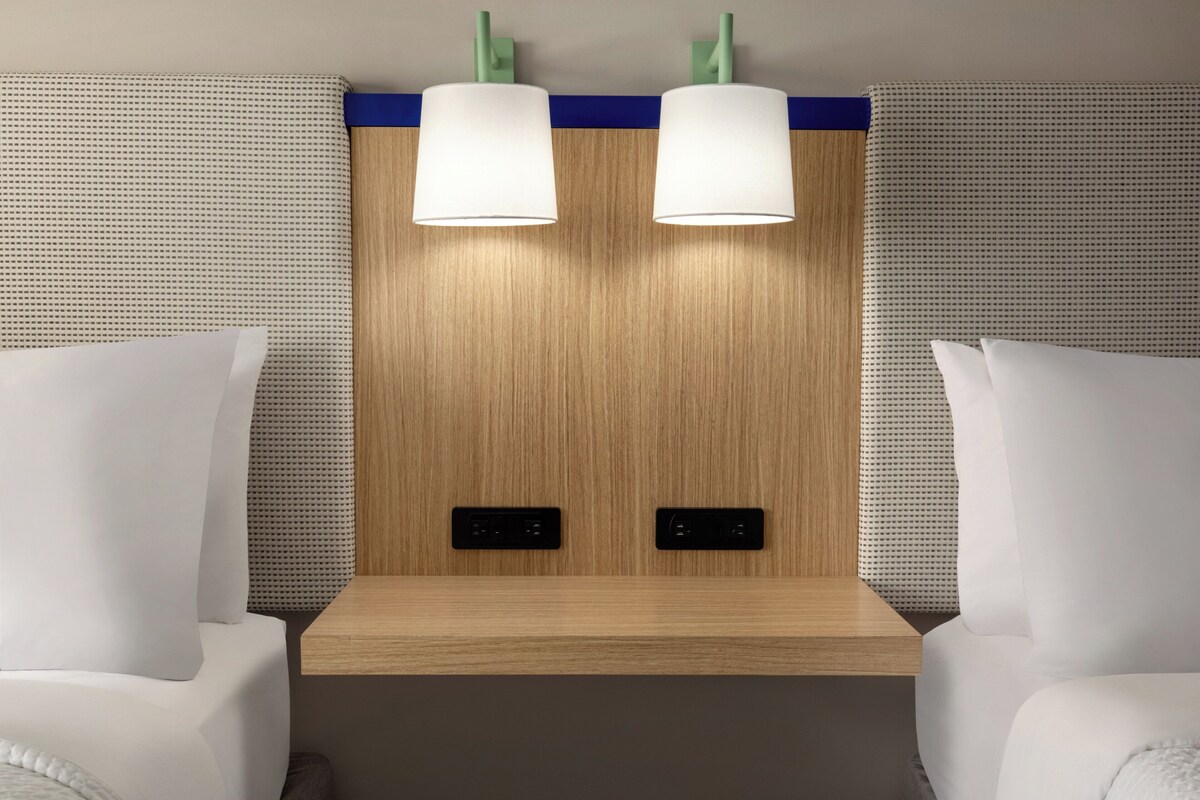Habitación de hotel con cabecera de madera, dos lámparas de noche y un panel de control.