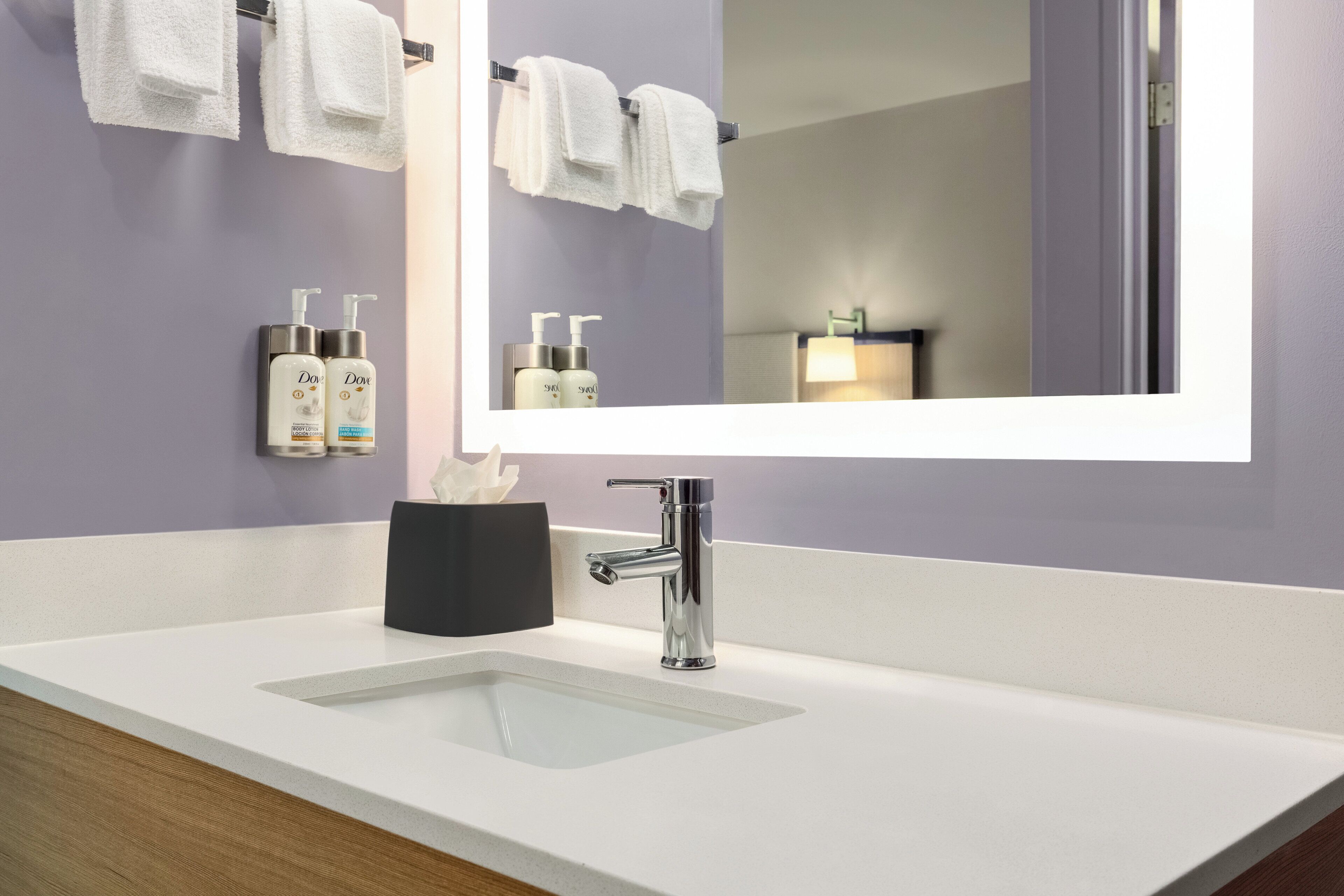 Un baño moderno con un lavabo blanco, un espejo grande y dos botellas de jabón Dove para el cuerpo.