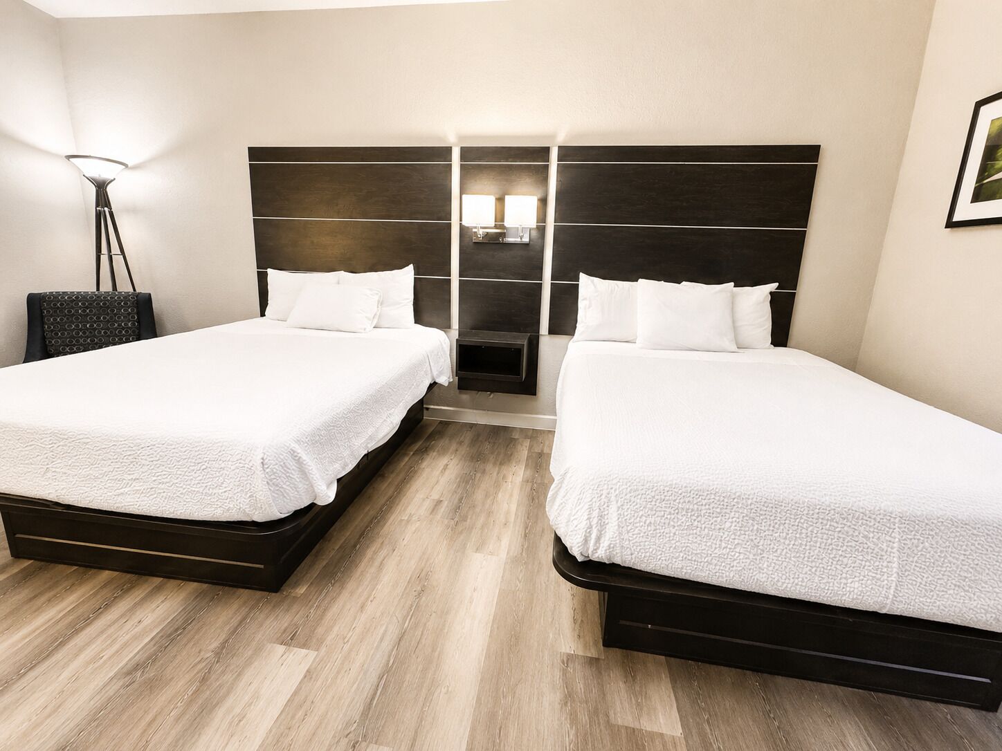 Habitación de hotel con dos camas, una mesita de noche, una lámpara y un estante fijado a la pared.