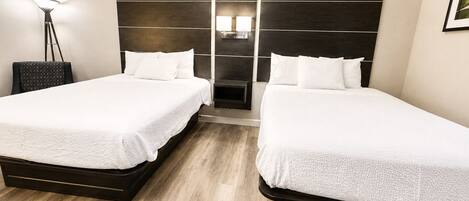 Habitación de hotel con dos camas, una mesita de noche, una lámpara y un estante fijado a la pared.