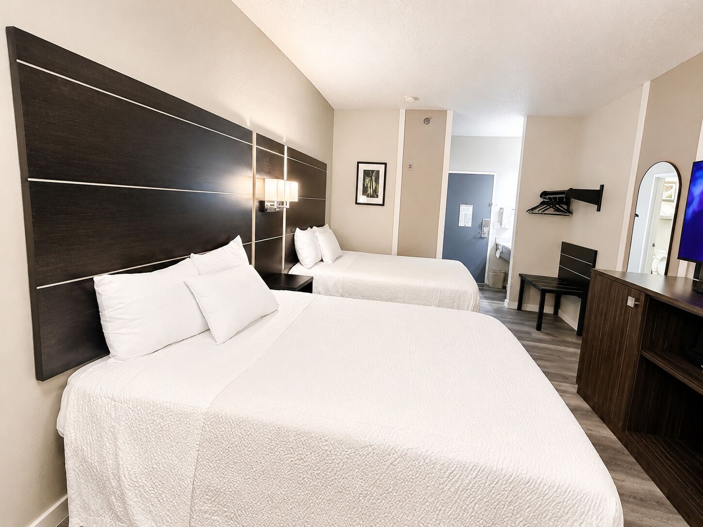 Habitación de hotel con dos camas, un escritorio, una silla, un televisor y un espejo.
