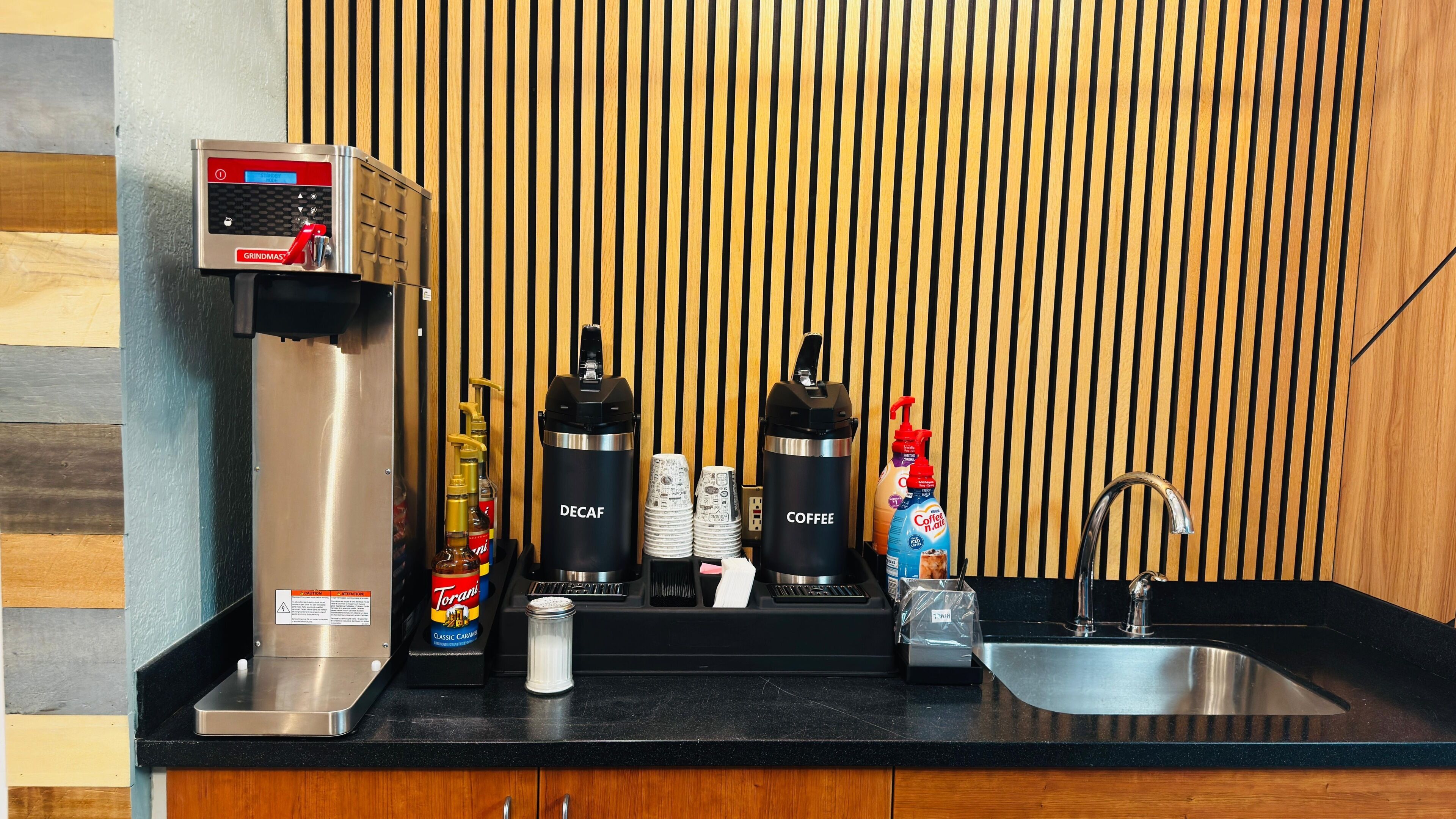En kaffestation med en kaffekvarn, två kaffedispensrar, Torani-sirap och en diskho.