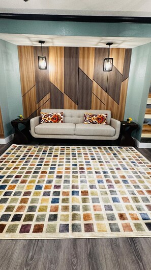 A room with a sofa, patterned rug, and a wall with geometric wooden paneling.