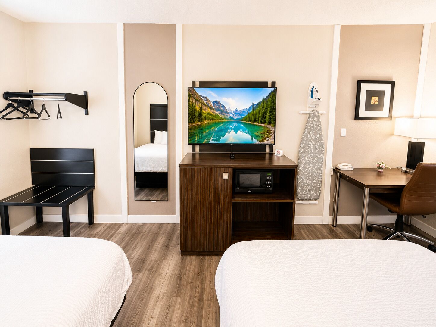 Hotelkamer met twee bedden, een televisie, bureau, stoel, spiegel, kapstok en magnetron.