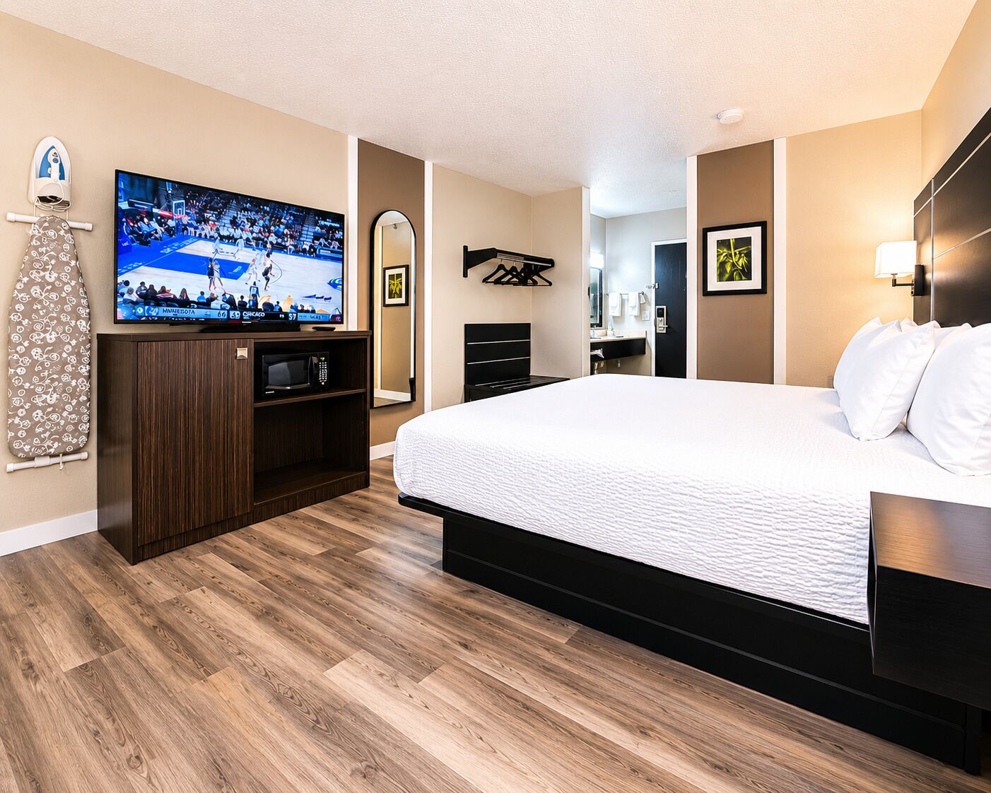 Habitación de hotel con una cama grande, televisión, espejo, armario y suelo de madera.