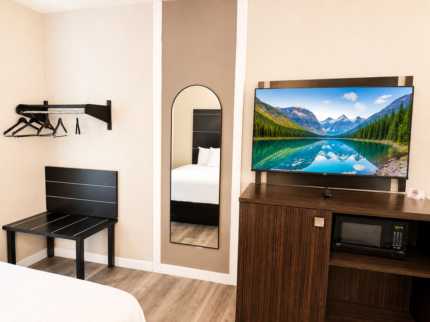 Une chambre d’hôtel équipée d’un lit, d’une télévision, d’un miroir, d’un porte-manteau et d’un four à micro-ondes.