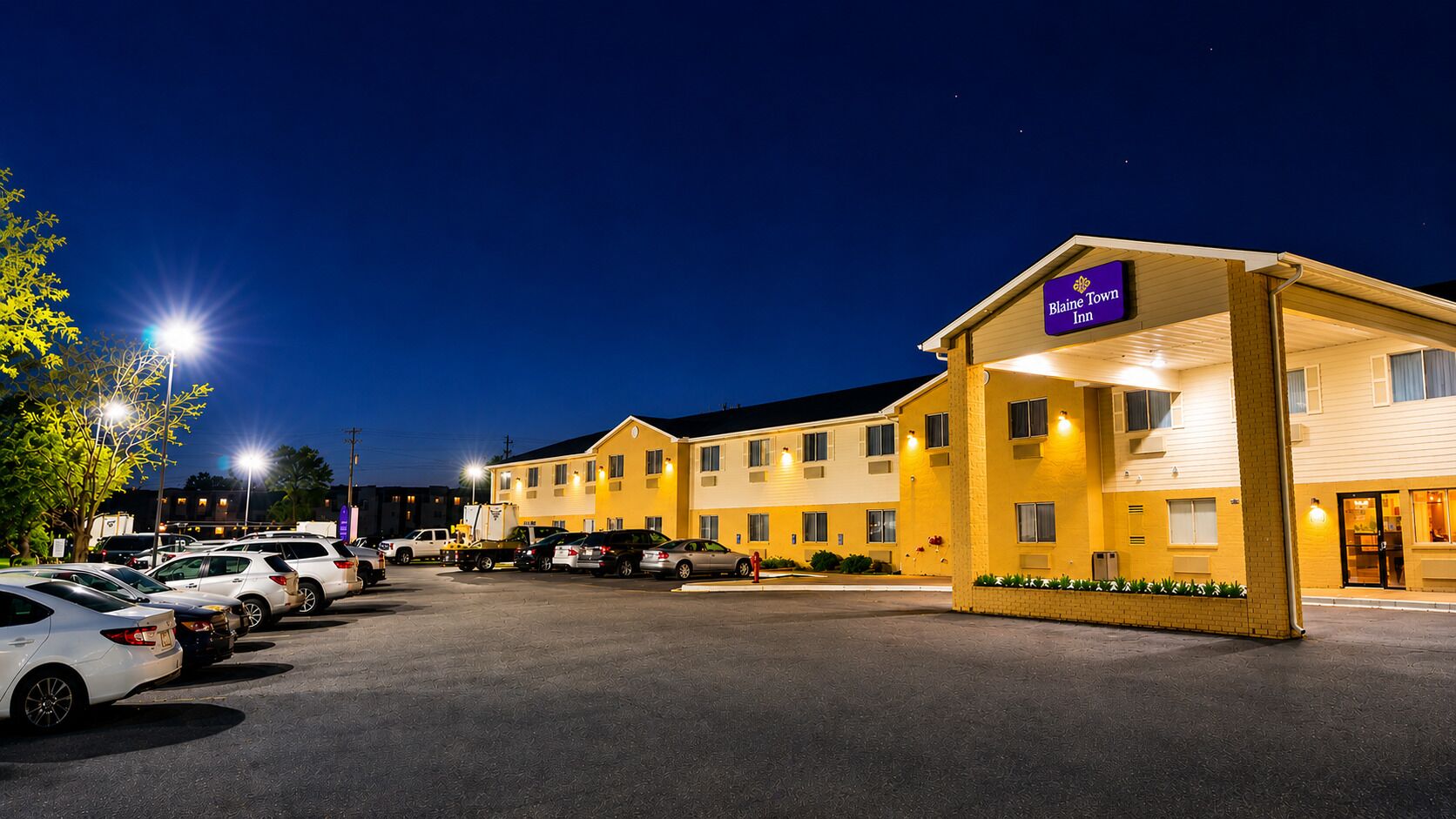 Un motel con un parcheggio, un edificio con il cartello che indica 'Blaine Tow Inn' e un ingresso ben illuminato.