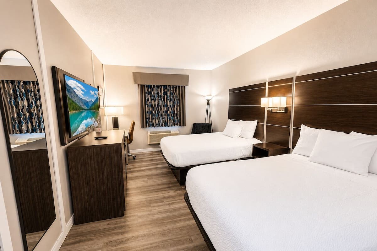Habitación de hotel con dos camas, un escritorio, un televisor y una ventana con cortinas.