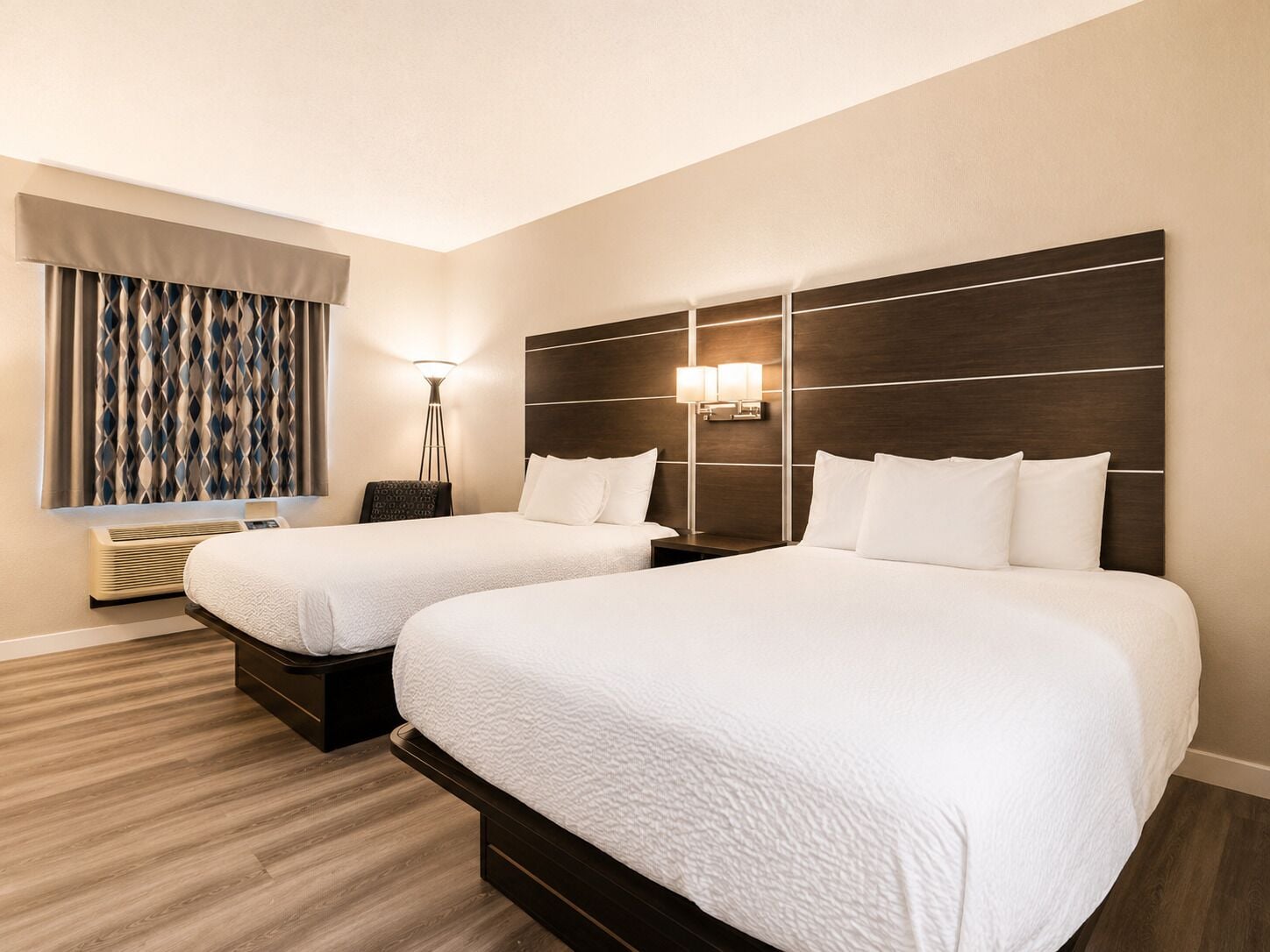 Ein Hotelzimmer mit zwei Betten, einer stehenden Lampe, einer Stehlampe und einem Fenster mit Vorhängen.
