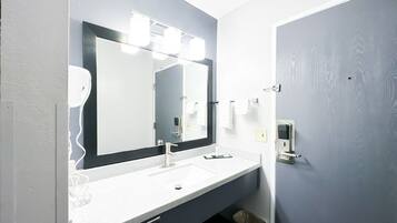 Une salle de bain avec un lavabo blanc, un miroir avec éclairage intégré, un distributeur de serviettes et une poubelle.