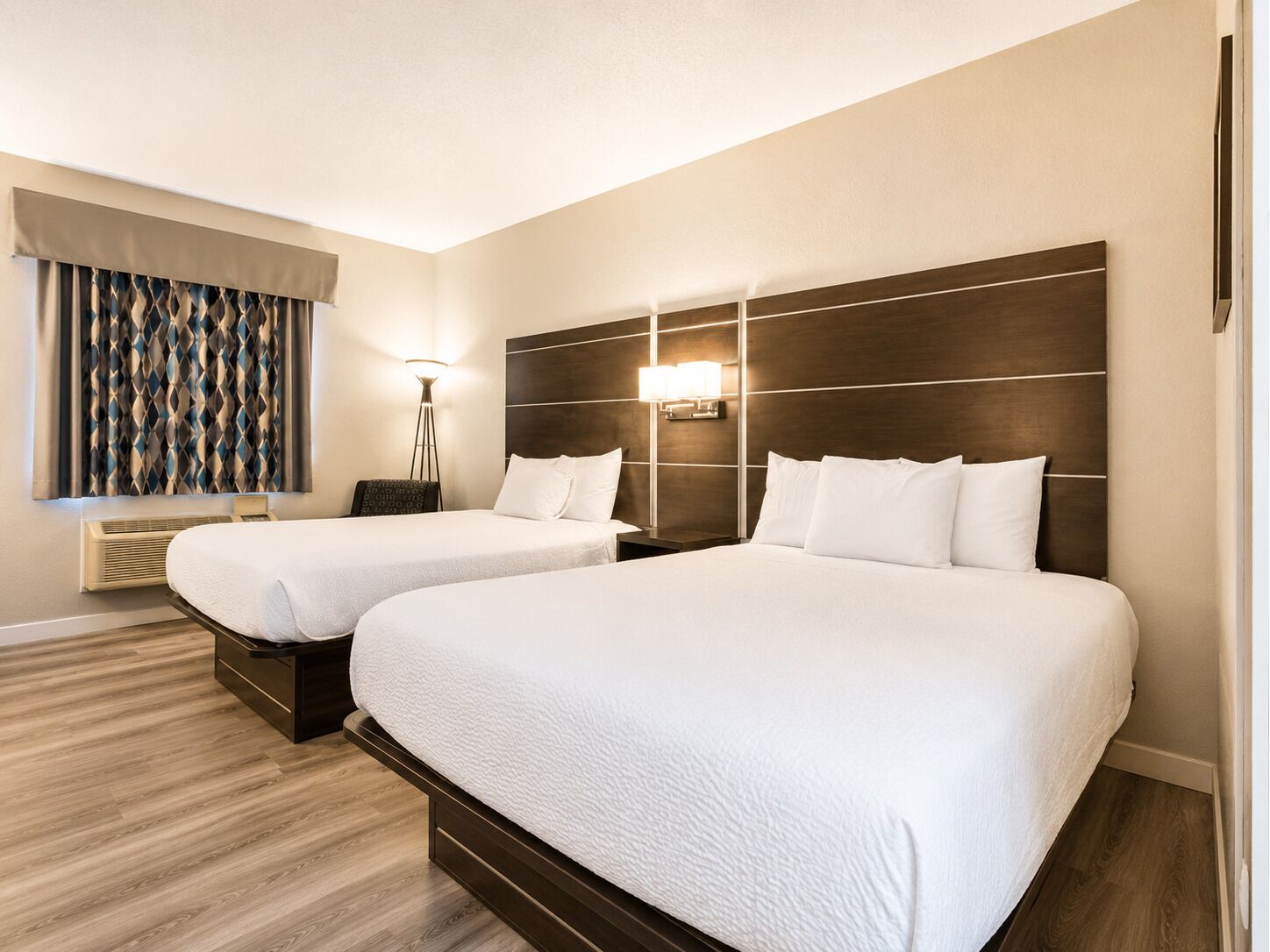 Een hotelkamer met twee bedden, een wandlamp en een raam met gordijnen met een patroon.