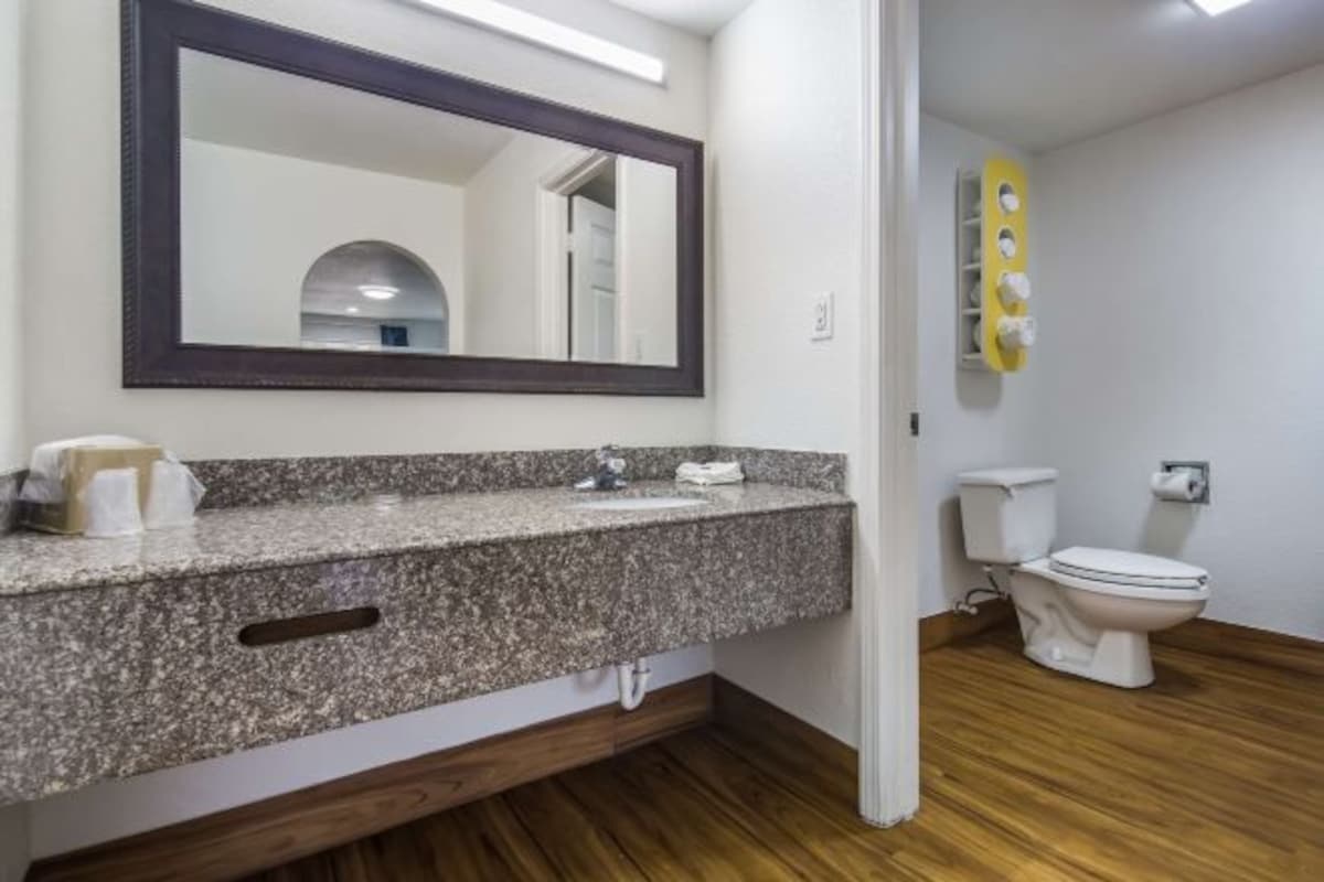 A bathroom with a granite countertop, a dark-framed mirror, a toilet, and a wooden floor.