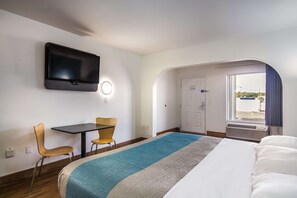 A hotel room with a bed, a desk with two chairs, a television mounted on the wall, and a door leading to a balcony. - Motel 6 Pensacola, FL - NAS (Pensacola)