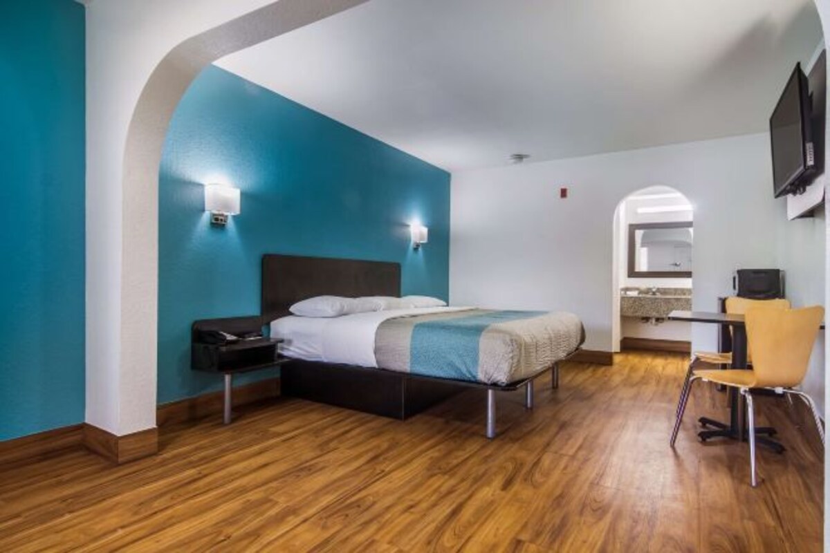 A modern hotel room with a bed, bedside table, and a desk with a chair.