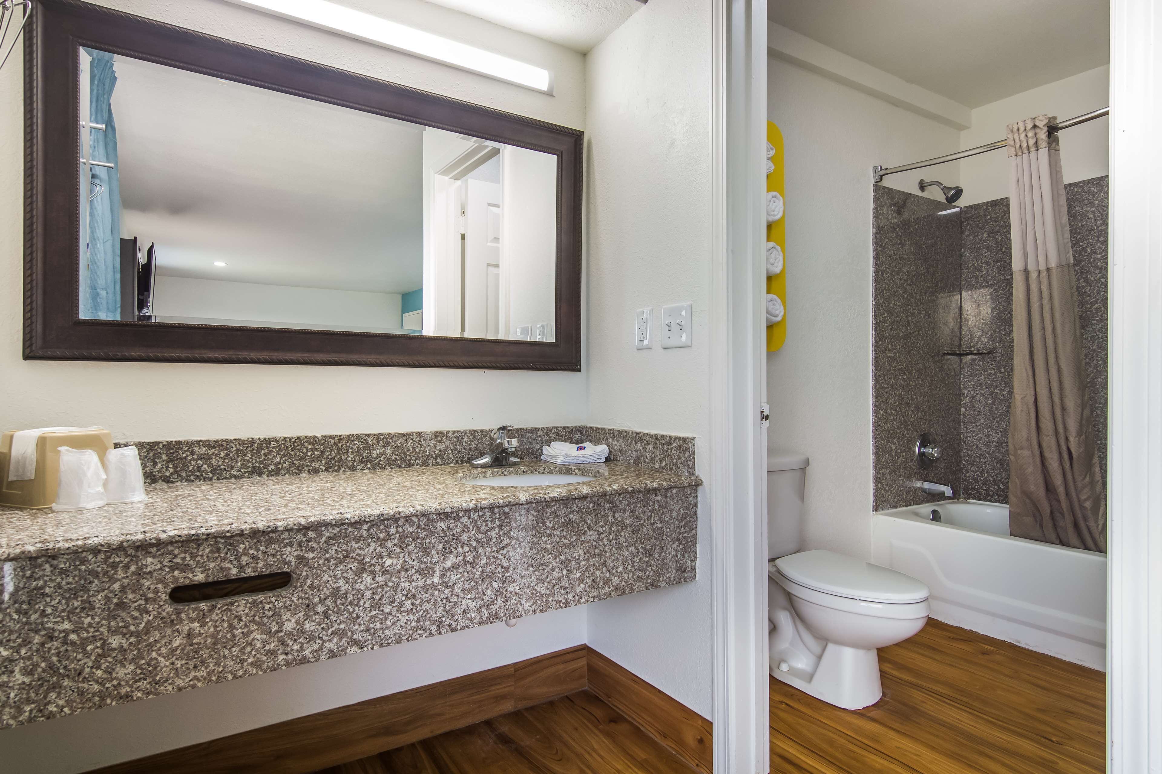 Une salle de bain avec un comptoir en granit, des toilettes blanches, une douche avec une porte en verre et un grand miroir au-dessus du lavabo.