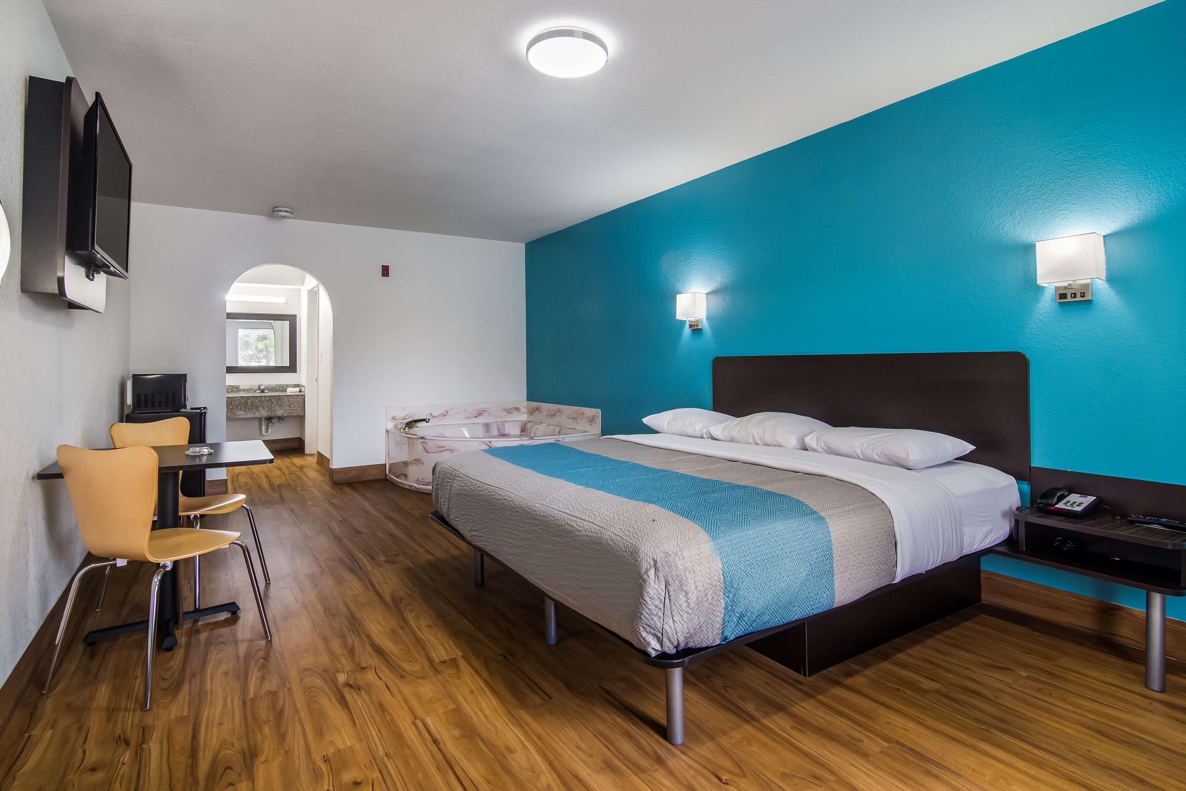 A hotel room with a bed, a desk, and a chair. There is a bathroom visible through an archway.