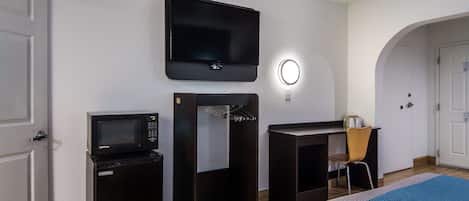 A hotel room with a bed, a TV mounted on the wall, a microwave, and a small desk with a chair.