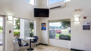 A reception area with a tiled floor, a flat-screen TV mounted on the wall, a small table with two chairs, and a large window offering a view of the outside.