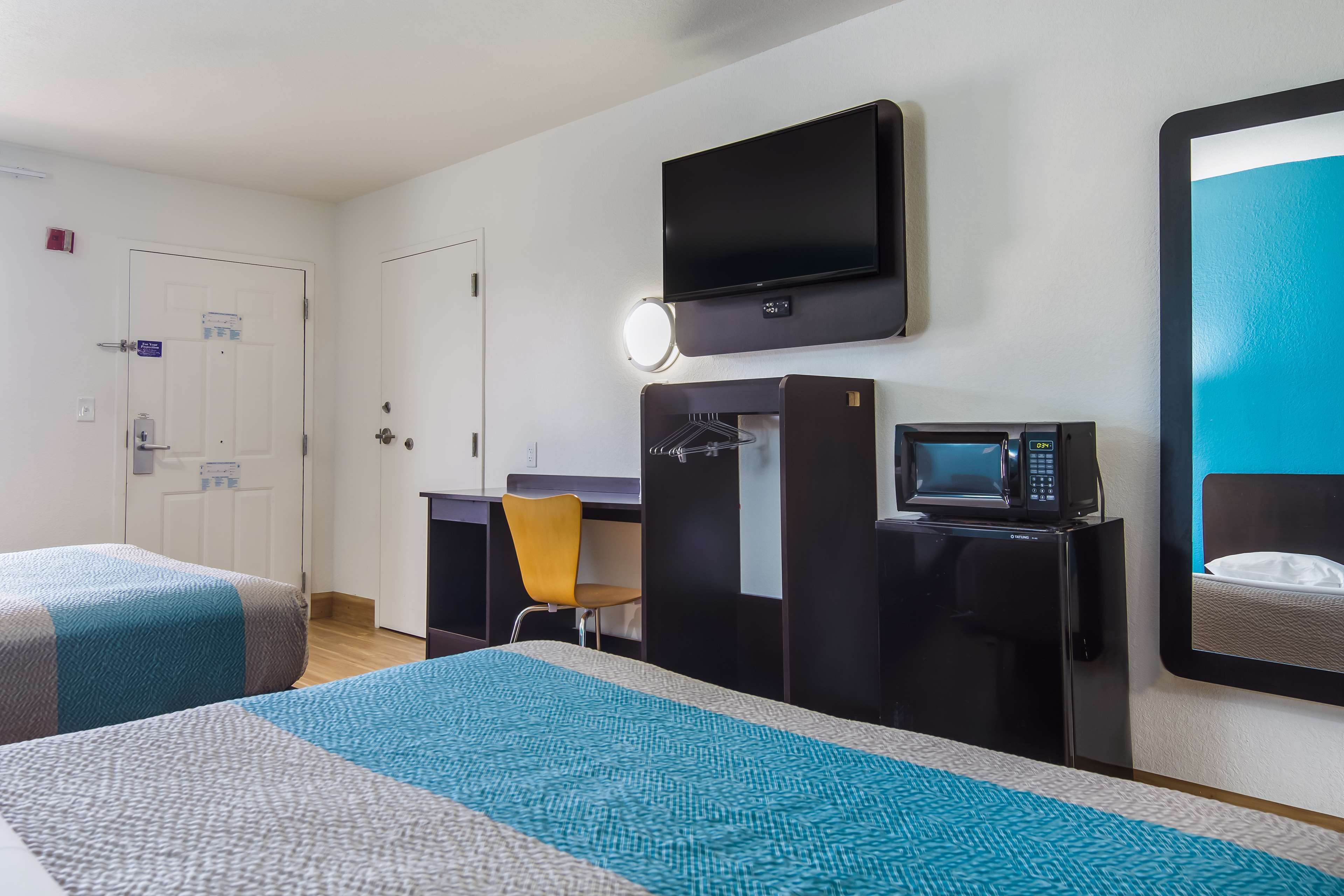 A hotel room with two beds, a desk with a chair, a TV, a microwave, and a refrigerator.