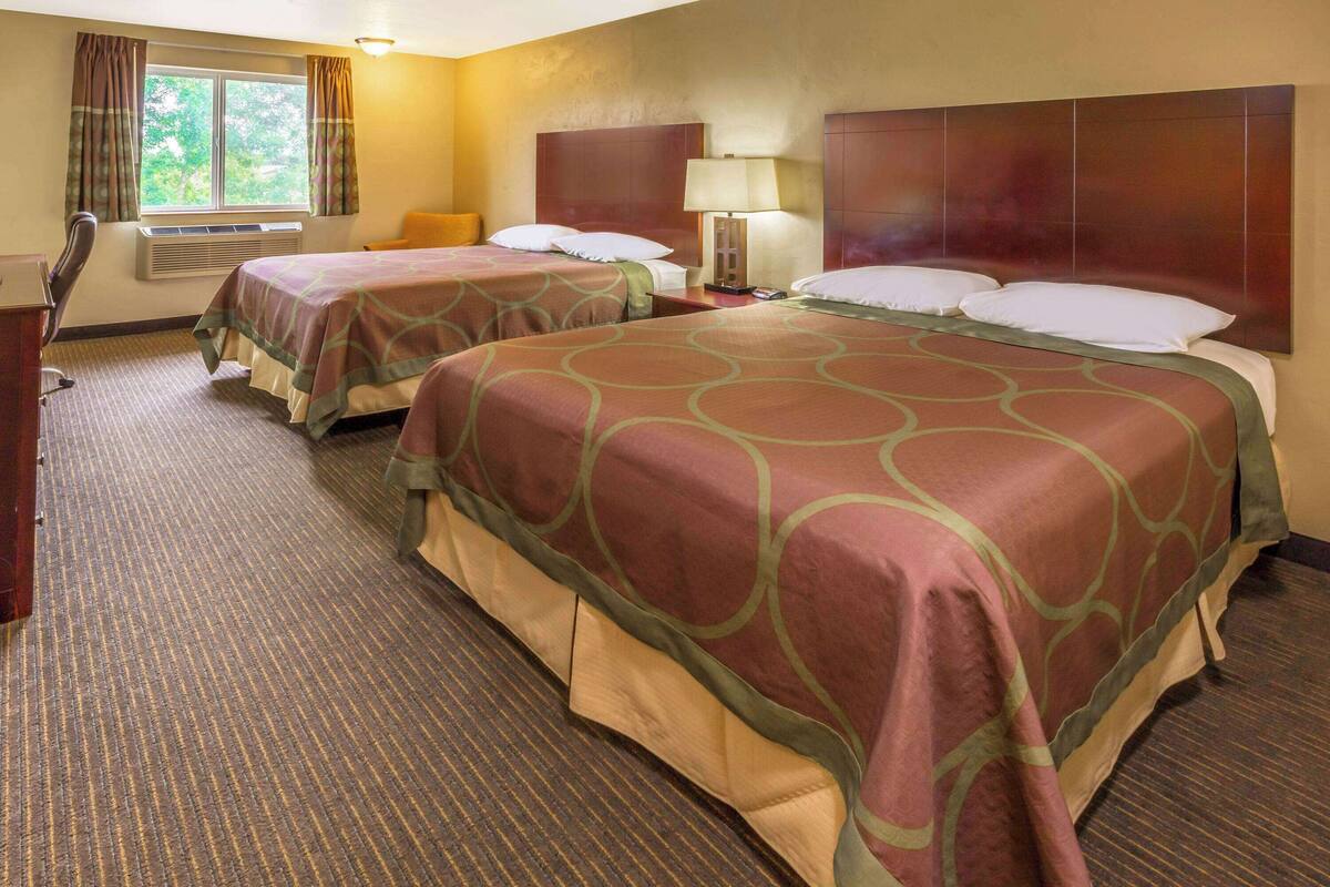 Een hotelkamer met twee bedden, een bureau, een stoel, een lamp en een raam met gordijnen.