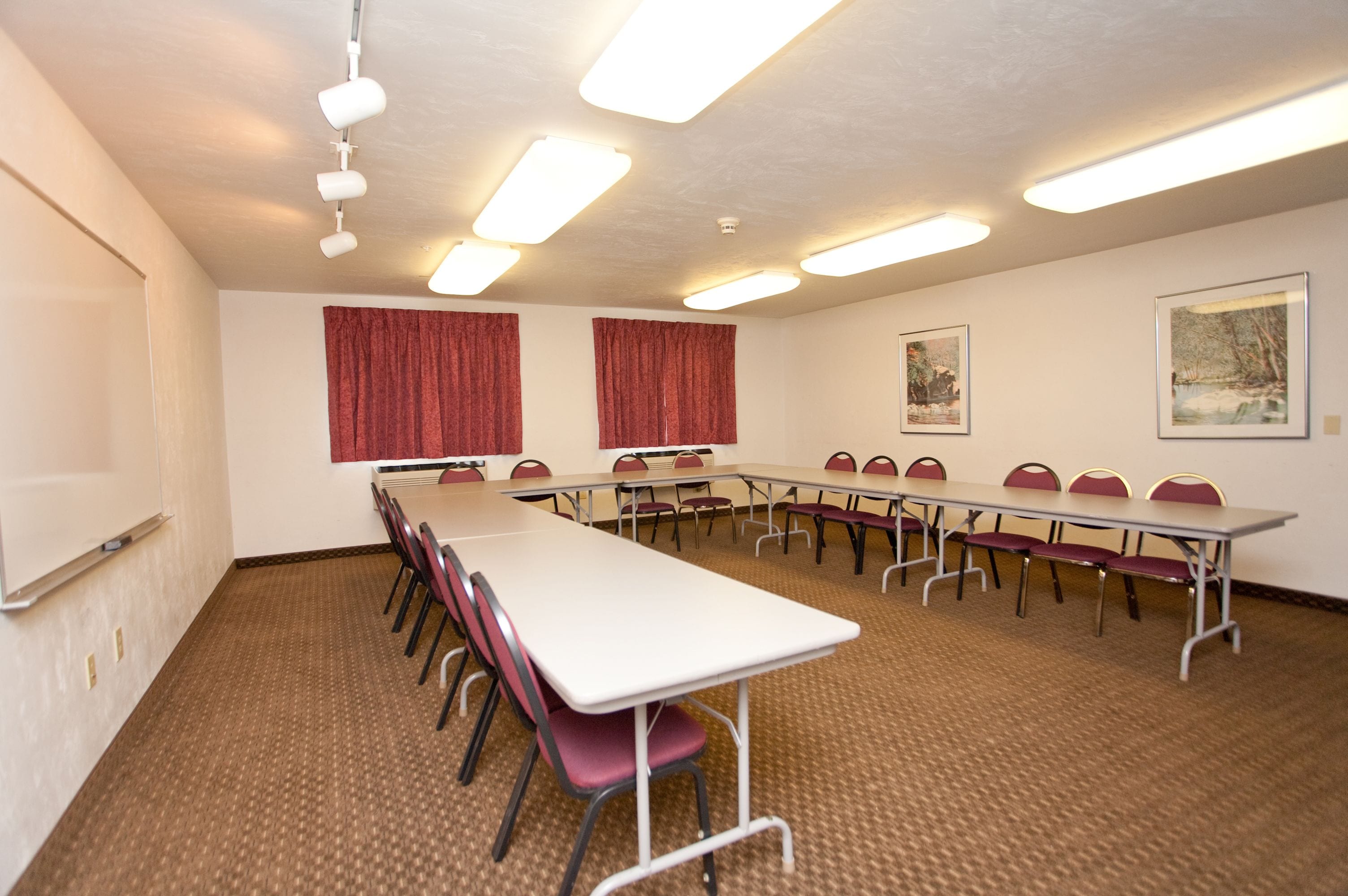 Un salón de conferencias con una larga mesa, sillas, cortinas rojas, cuadros en la pared y luces en el techo.