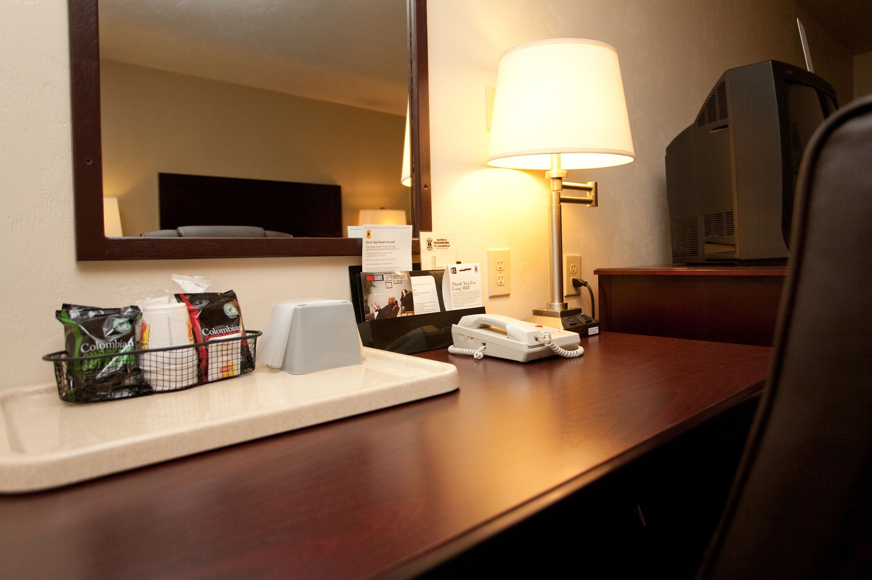A hotel room desk with a lamp, a telephone, a television, and a tray with toiletries.