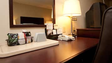 A hotel room desk with a lamp, a telephone, a television, and a tray with toiletries.