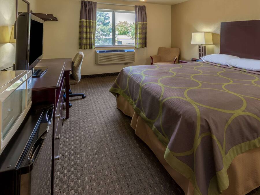 A hotel room with a bed, a desk with a television, a chair, and a window with curtains.