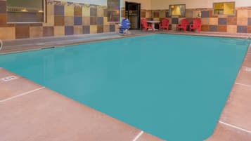 A swimming pool with red chairs and a table, surrounded by tiled walls.