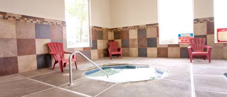 A spa area with a hot tub, tiled walls, and red chairs.