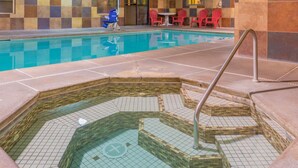 Una piscina con zona de hidromasaje, sillas rojas y una silla azul.