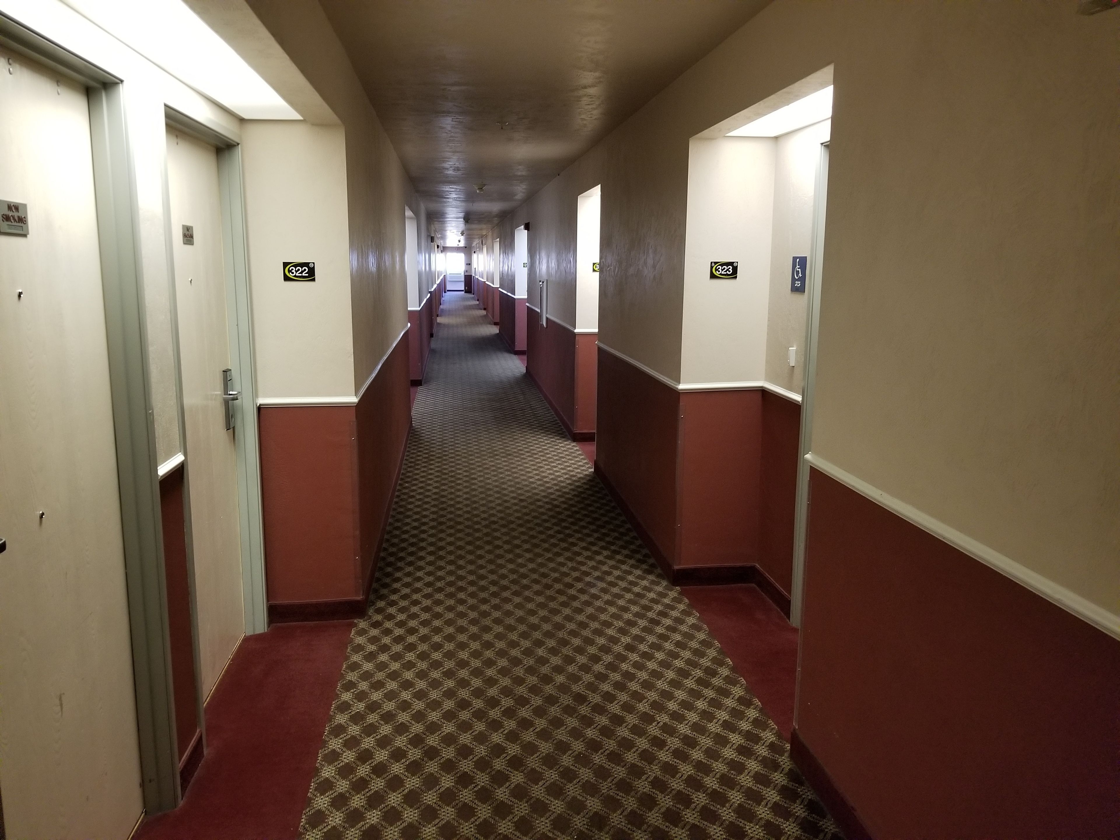 A long, narrow hotel corridor with carpeted floors and alternating red and beige walls.