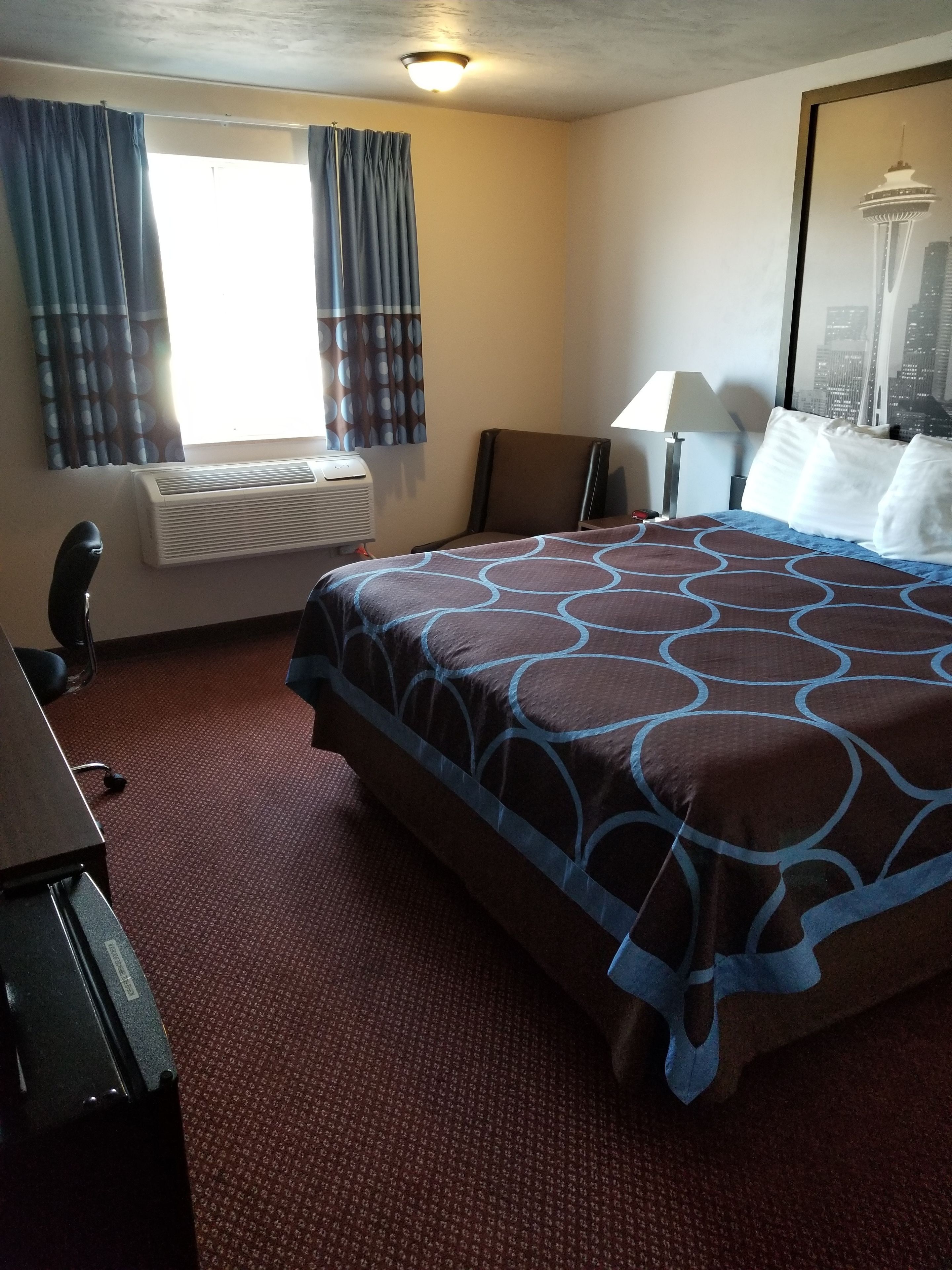 A hotel room with a large bed, a desk, a chair, a lamp, and a window with curtains.