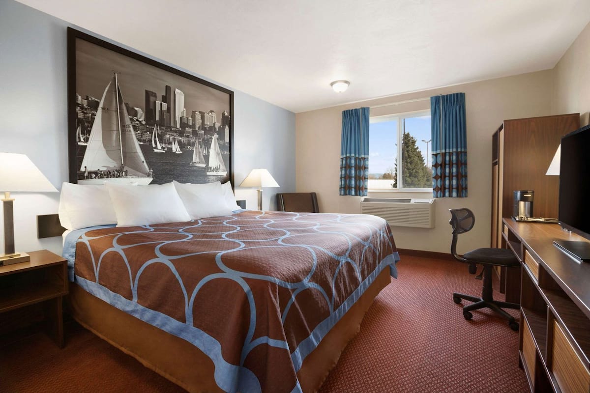 A hotel room with a bed, desk, chair, television, and a large cityscape painting on the wall.