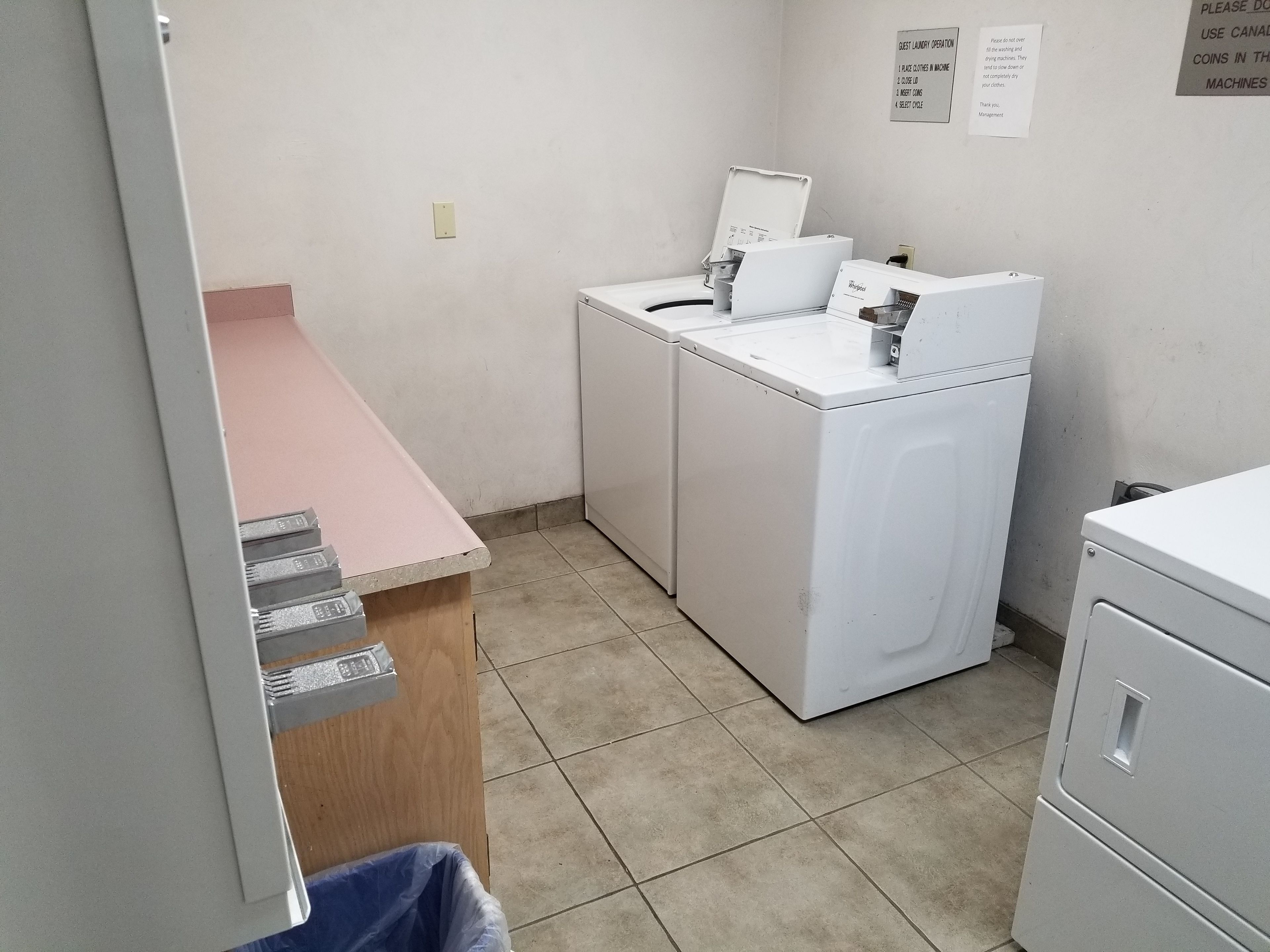A laundry area with a washing machine, dryer, and a counter with a trash bin.