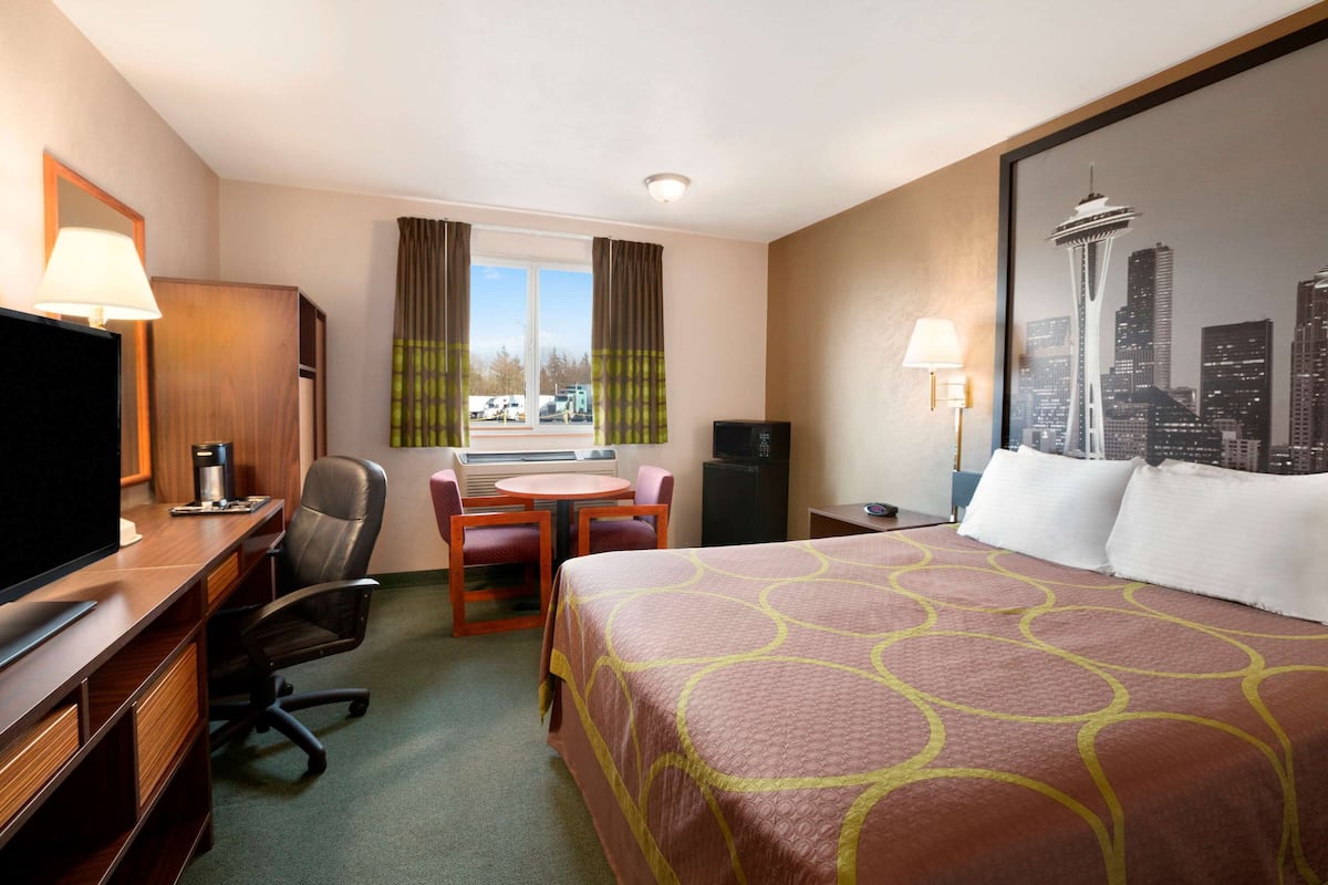 A hotel room with a bed, desk, chair, and a view of the cityscape including a tower.
