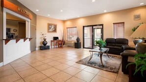 A reception area with a 'WELCOME' sign, a reception desk, a seating area with a sofa and armchairs, a coffee table, and a large window with blinds. - Super 8 by Wyndham Bellingham Airport/Ferndale (Ferndale)