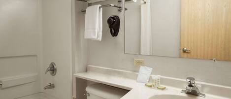 Un baño moderno con bañera, lavabo e inodoro. Se ve un toallero con toallas dobladas y un secador de pelo negro.