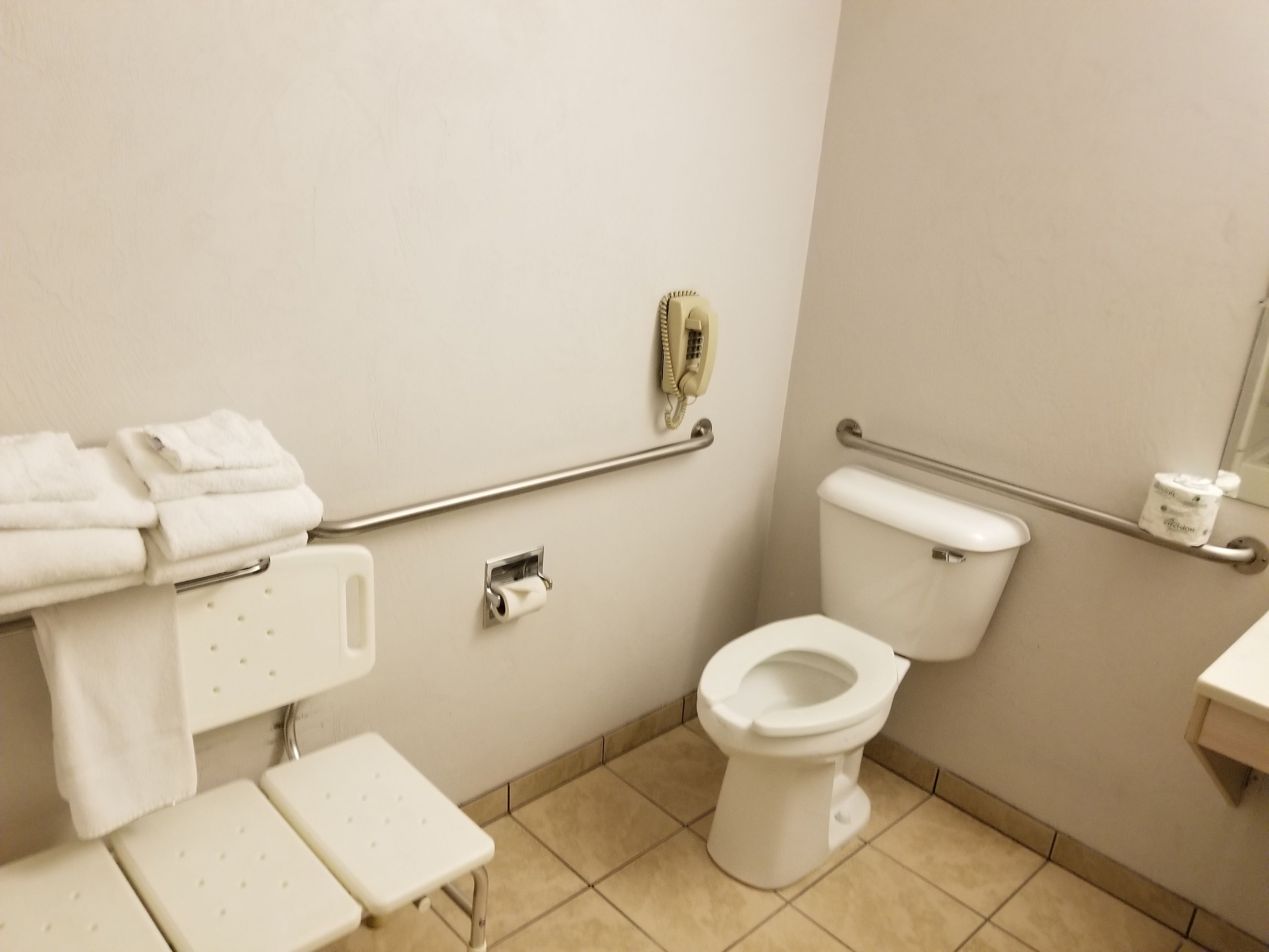 A bathroom with a toilet, handrails, a small table, and a towel rack.