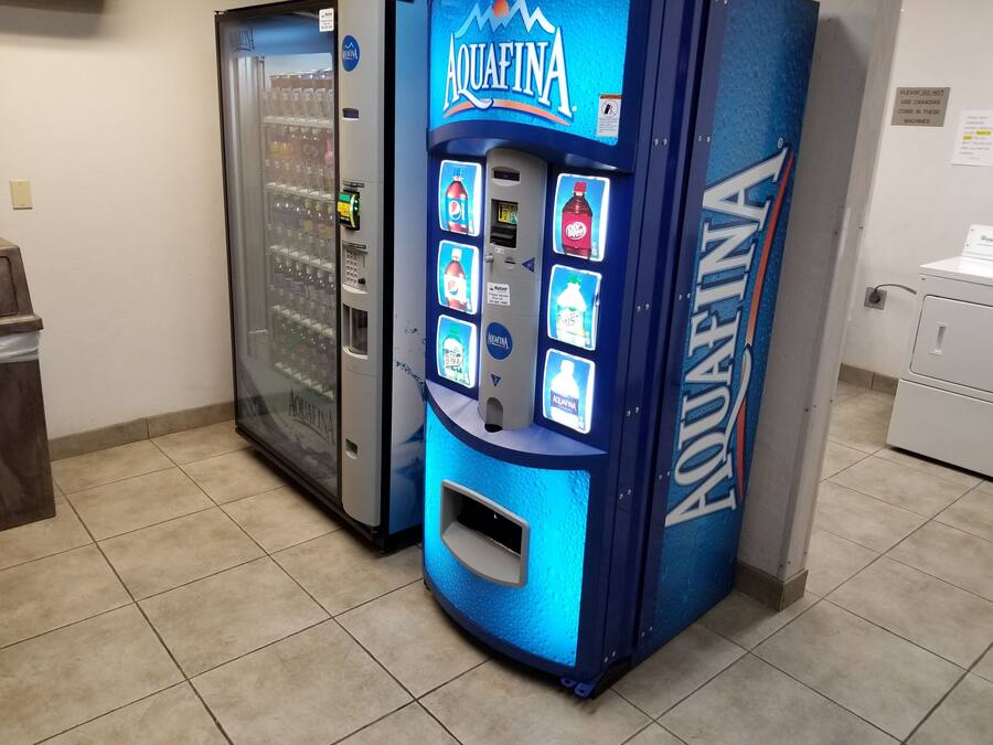 Máquina expendedora con varias opciones de bebidas, incluyendo agua Aquafina, y un refrigerador.