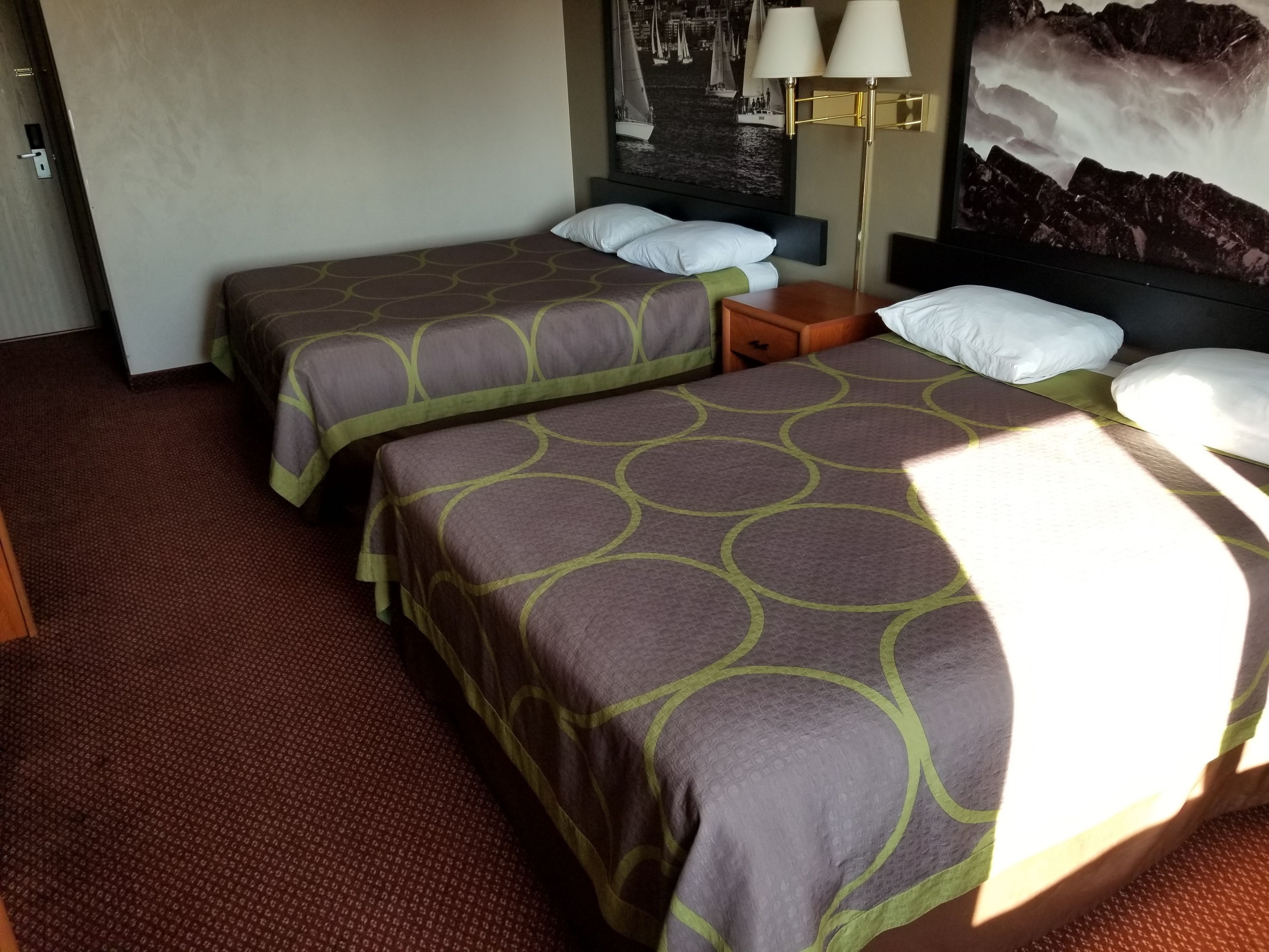 A hotel room with two beds, a nightstand, a lamp, and a painting of a seascape.