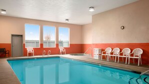 A swimming pool with clear blue water, surrounded by white chairs, and large windows with a view of the sky and trees. - Super 8 by Wyndham Bellingham Airport/Ferndale (Ferndale)