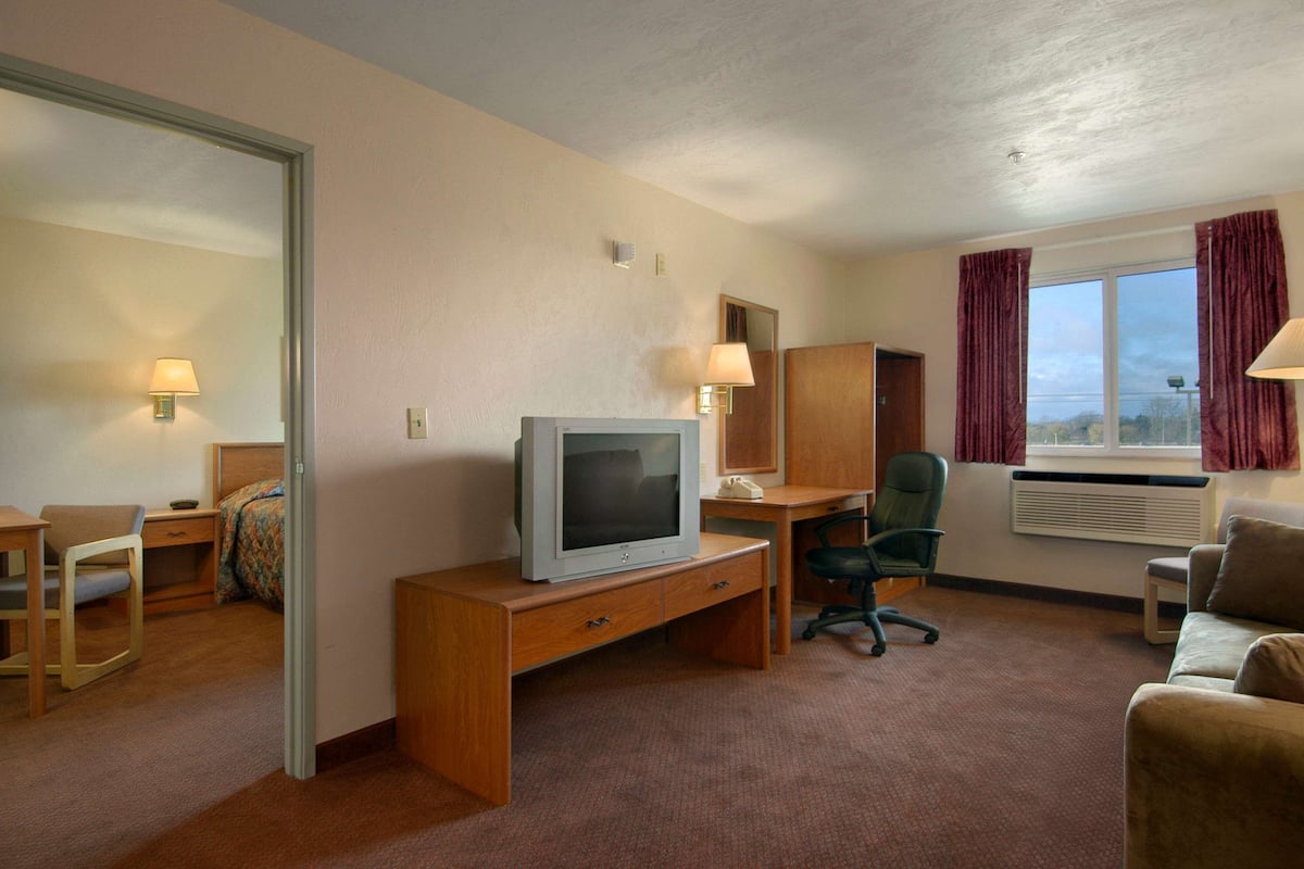 A hotel room with a desk, chair, TV, and a couch.