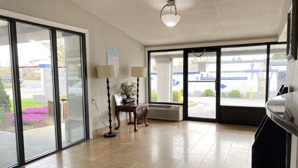 A spacious lobby with a large sliding glass door, a wooden table with lamps, and a ceiling light fixture. - Travelodge by Wyndham Laurel/Ft. Meade/Near NSA (Laurel)