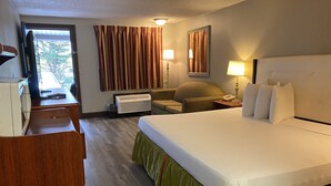 A hotel room with a bed, a desk, a chair, a TV, an air conditioner, and a window with curtains. - Travelodge by Wyndham Laurel/Ft. Meade/Near NSA (Laurel)