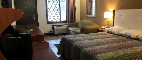 Habitación de hotel con cama, escritorio, silla, lámpara y ventana con cortinas.