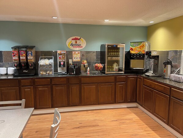 A breakfast bar with various food and drink dispensers, including a coffee machine and a refrigerator. - Super 8 by Wyndham Monroe (Monroe)