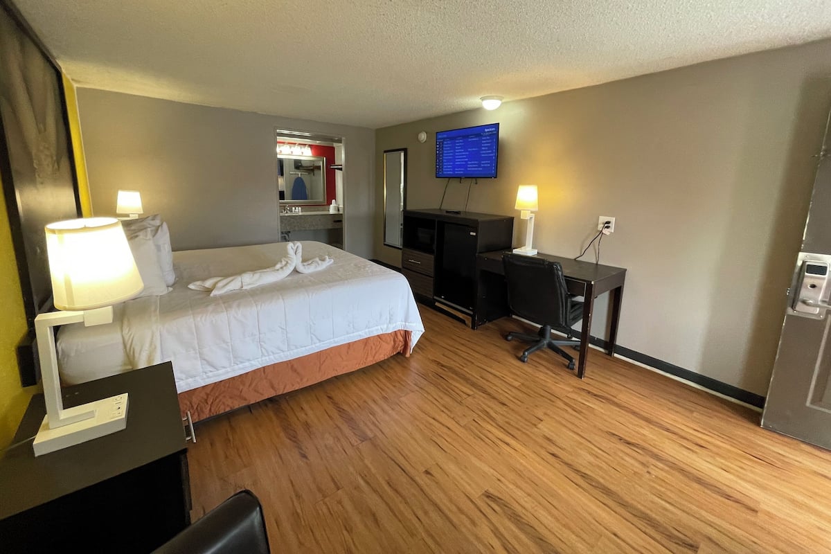 A hotel room with a bed, desk, computer, TV, and a bathroom mirror.